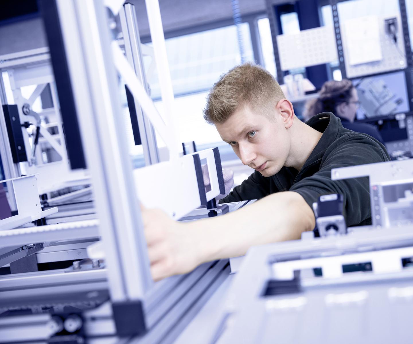 Ein junger Mann arbeitet konzentriert an einer technischen Vorrichtung in einer modernen Arbeitsumgebung.