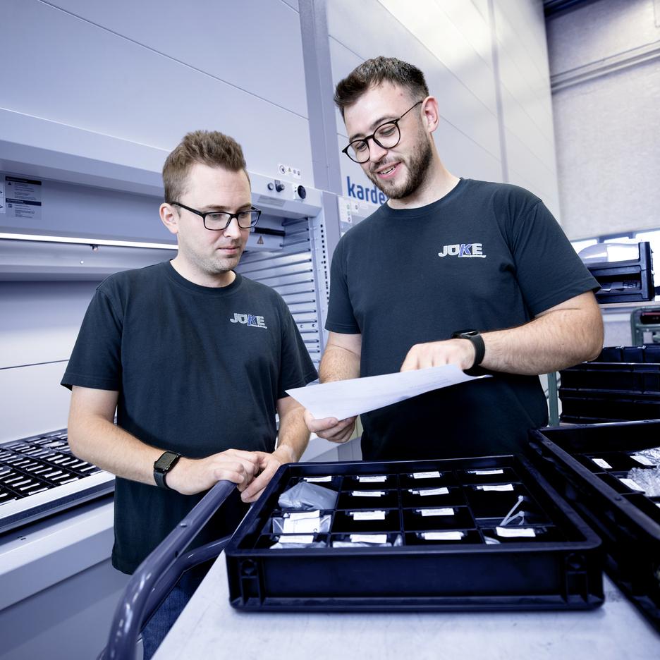 Zwei Mitarbeiter betrachten ein Dokument vor einem Regal mit Aufbewahrungsboxen in einem modernen Lager.