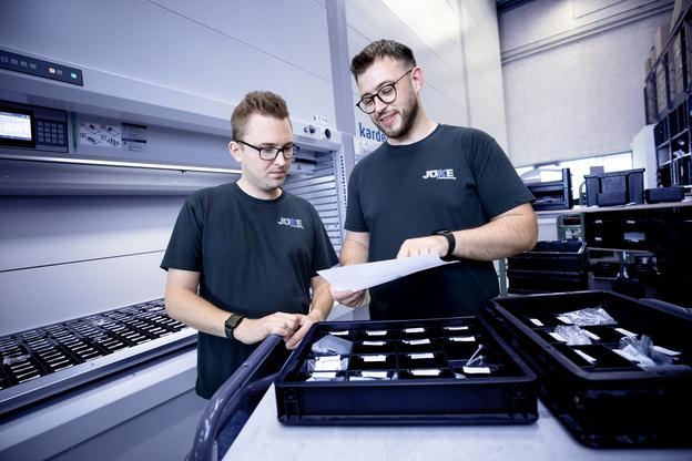 Zwei Mitarbeiter betrachten ein Dokument vor einem Regal mit Aufbewahrungsboxen in einem modernen Lager.